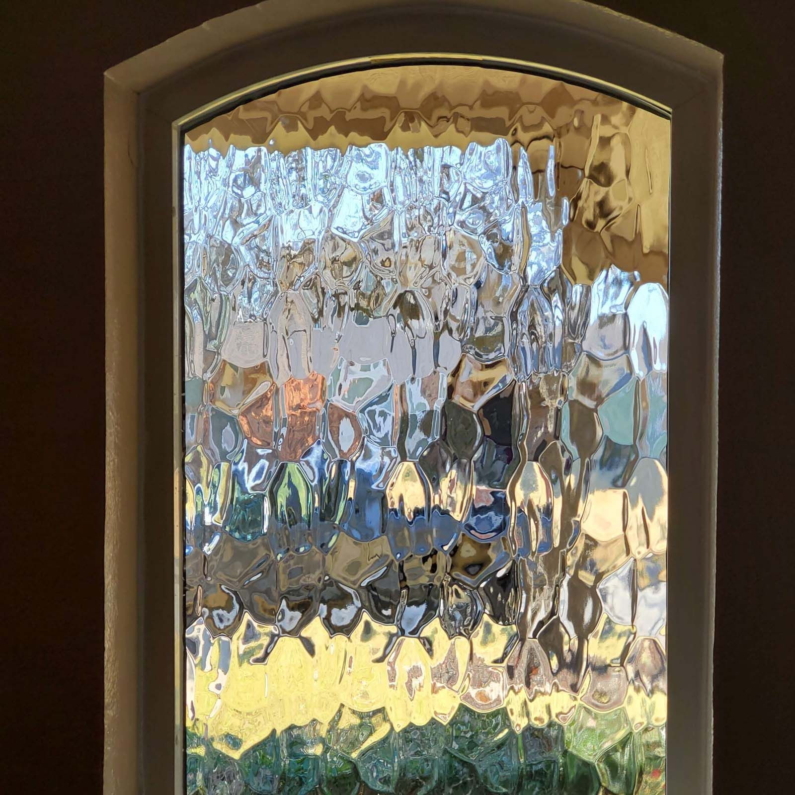 Textured glass window, arched top, framed in white.  Blurred view of outdoors through the glass.