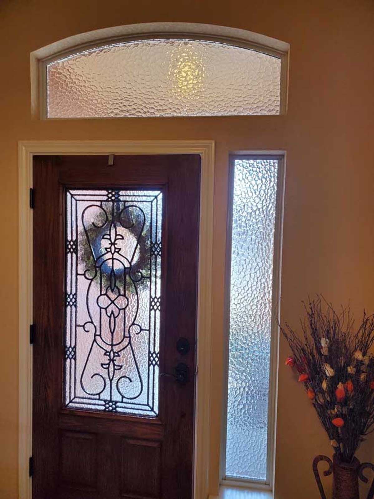 Wooden front door with decorative glass, sidelight, and arched transom window.