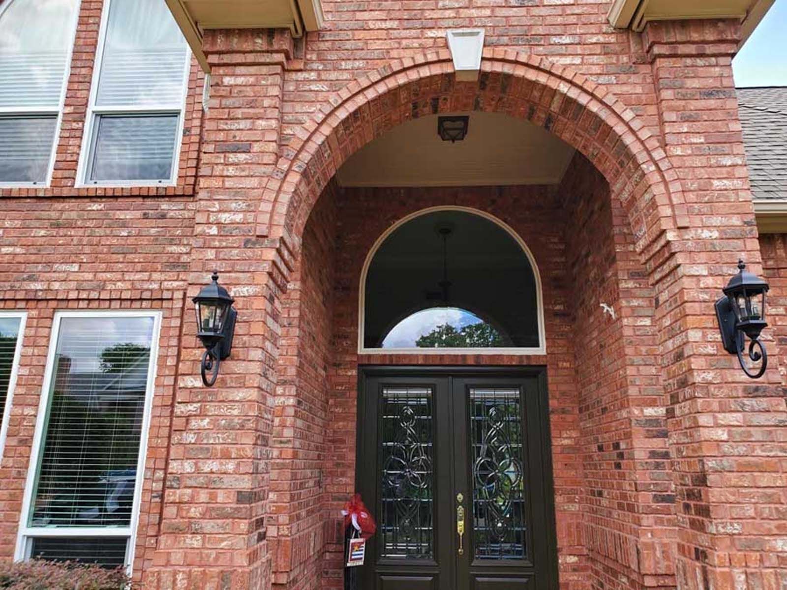 Brick home entrance with arched doorway, dark double doors, and black sconces.
