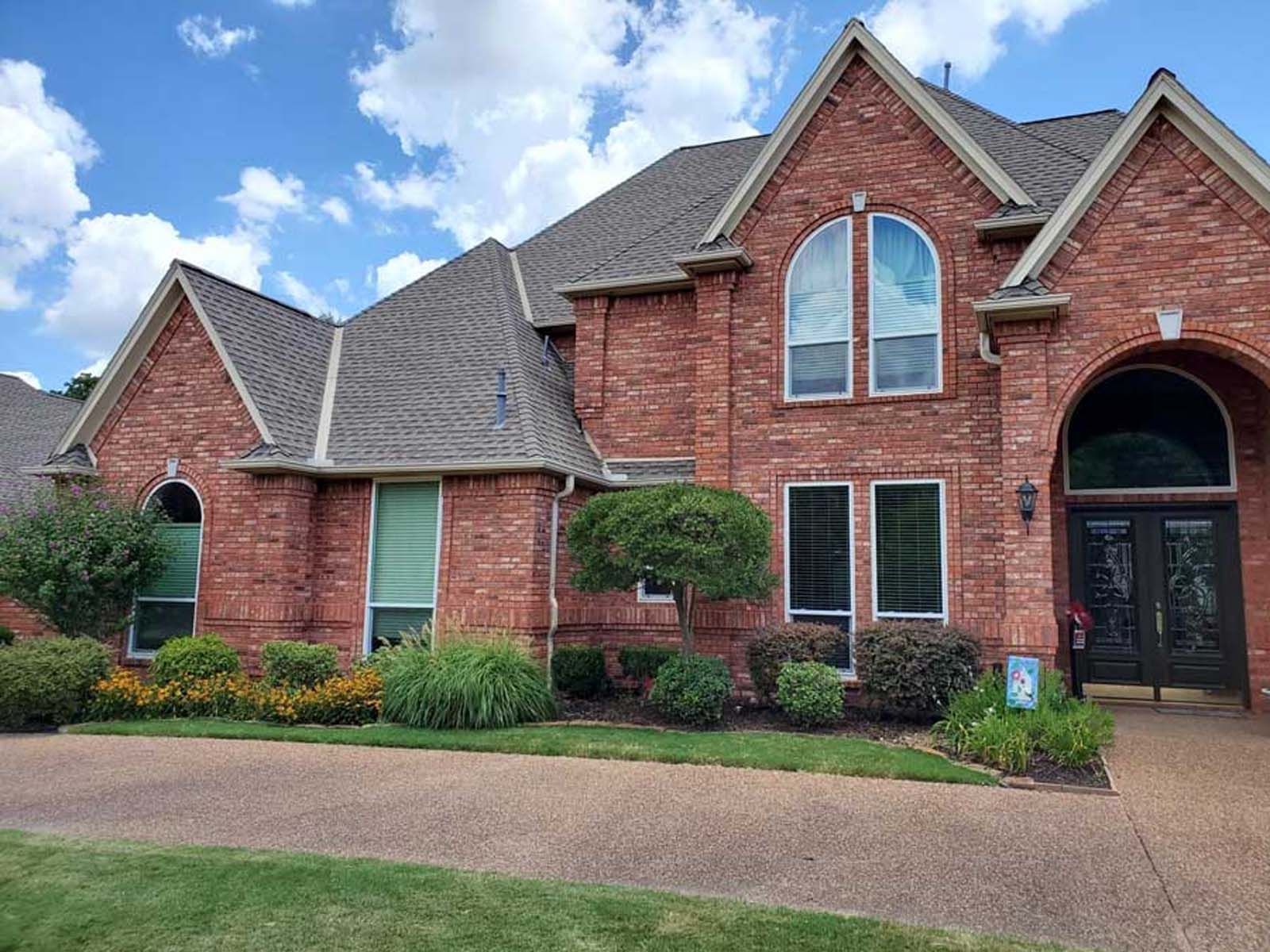 Red brick house with dark roof, arched doorway, and landscaped front yard.