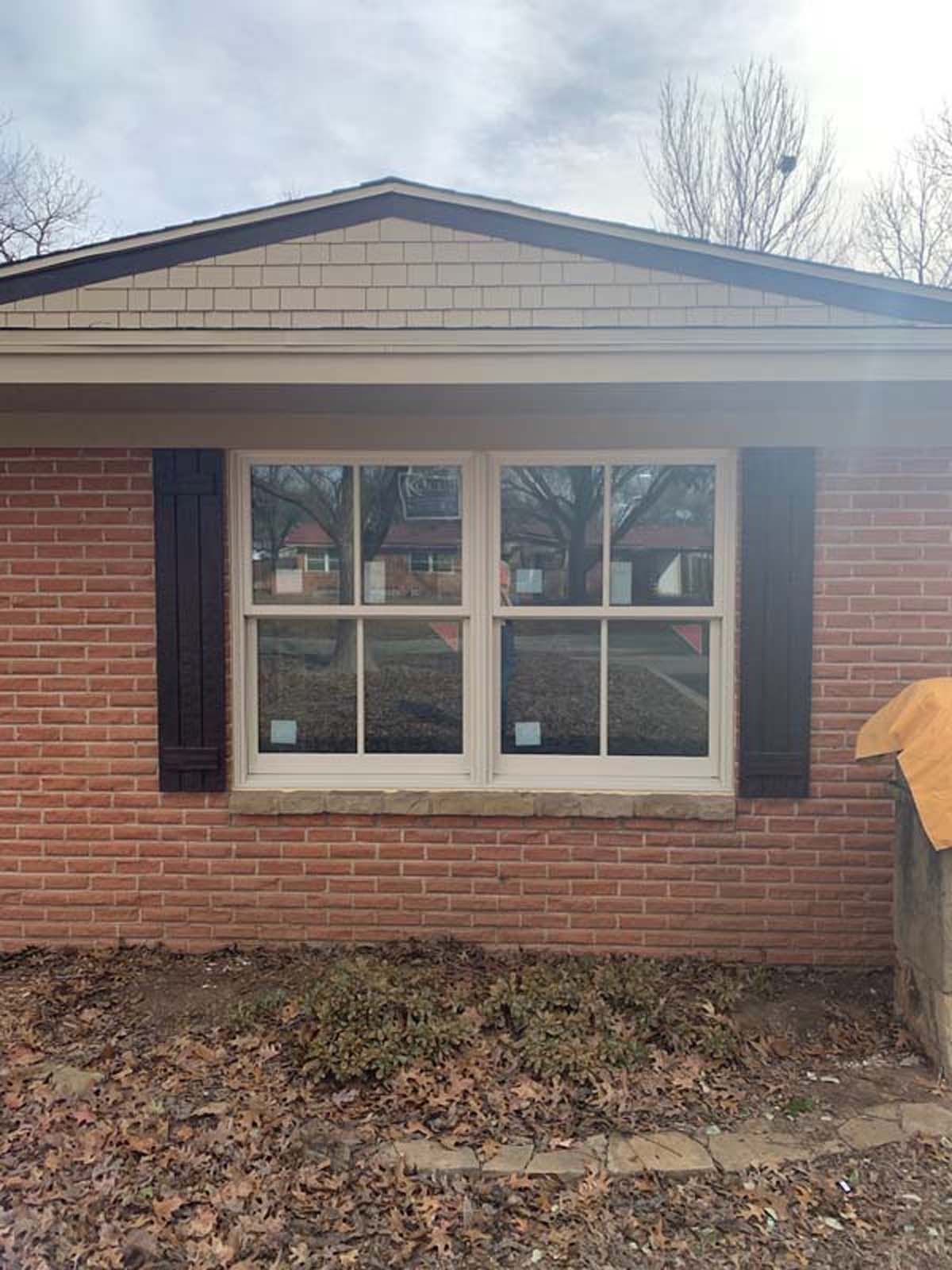 Red brick house with white-framed window, brown shutters, and cedar shake gable.