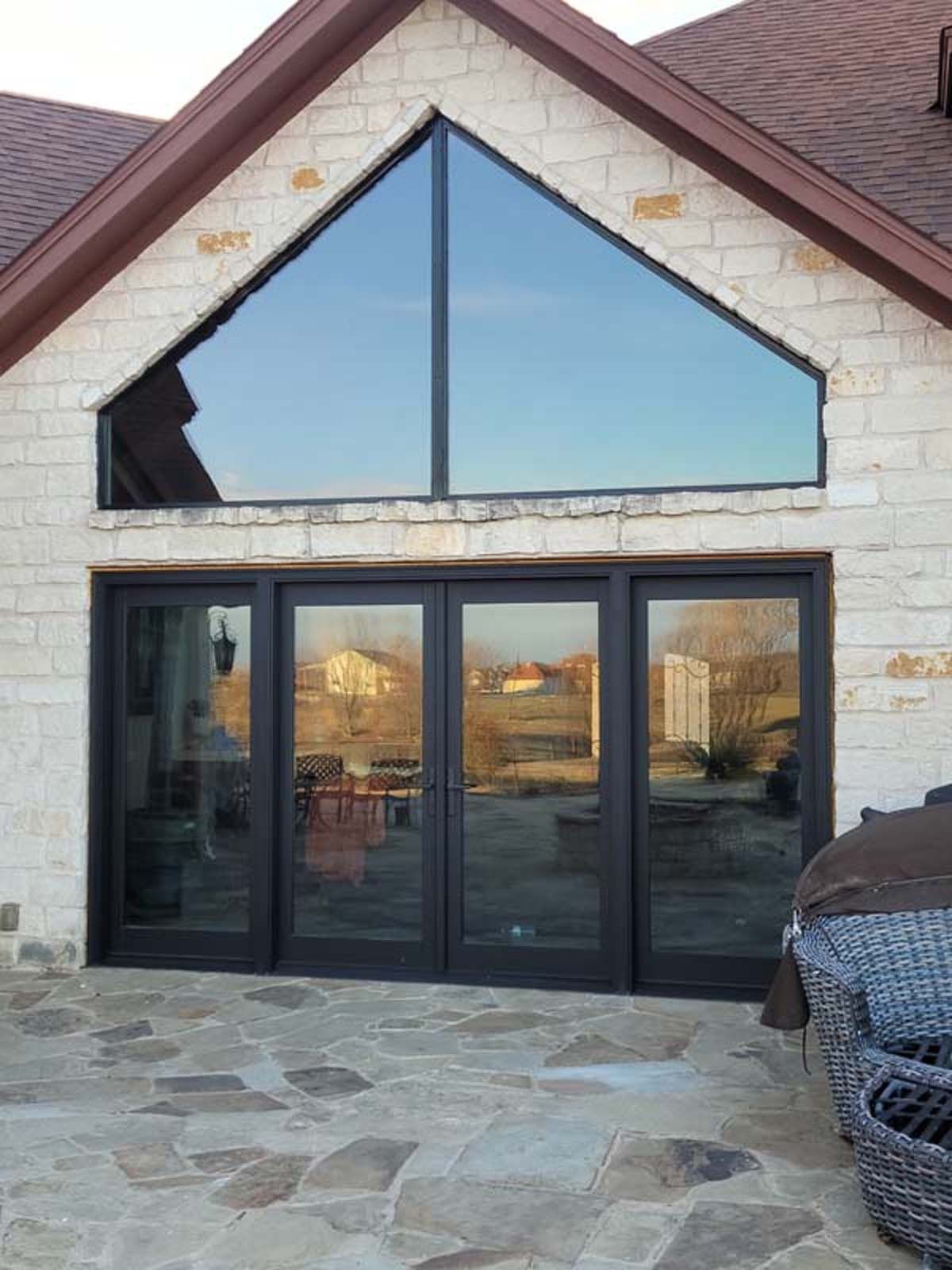 Exterior view of a house with large windows and doors, stone facade, and a patio.