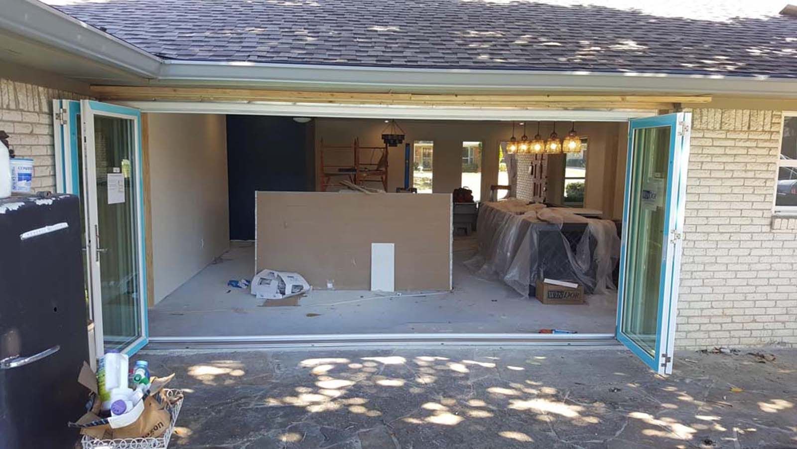 Open folding doors reveal a room under renovation. Drywall, tools, and a dining table are visible.