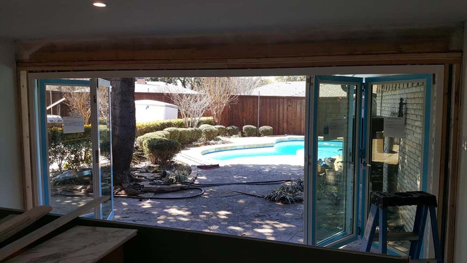 Open glass folding doors overlooking a backyard with a pool.