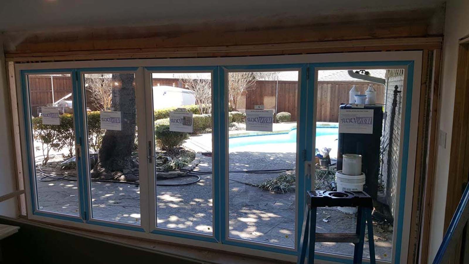 New multi-pane window with blue tape, overlooking a backyard with a pool.