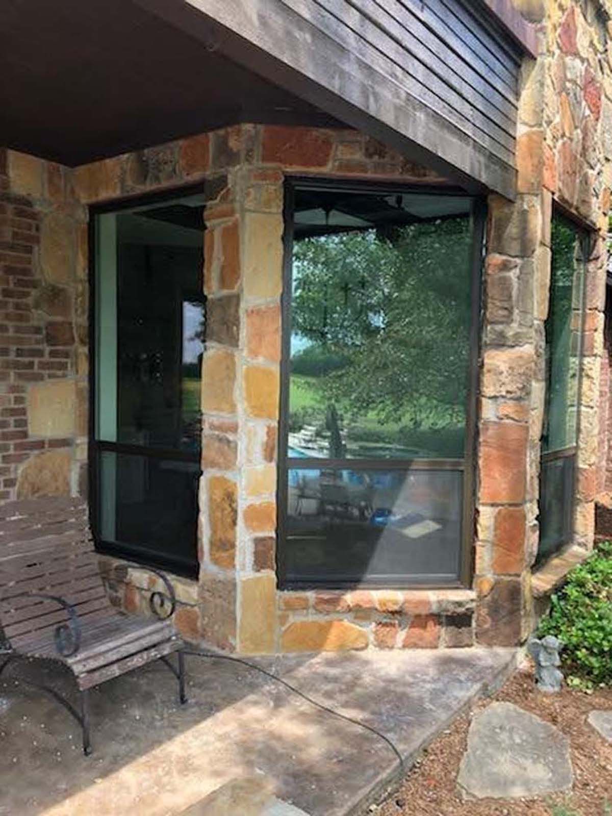 Stone exterior corner with large windows, a chair, and greenery.