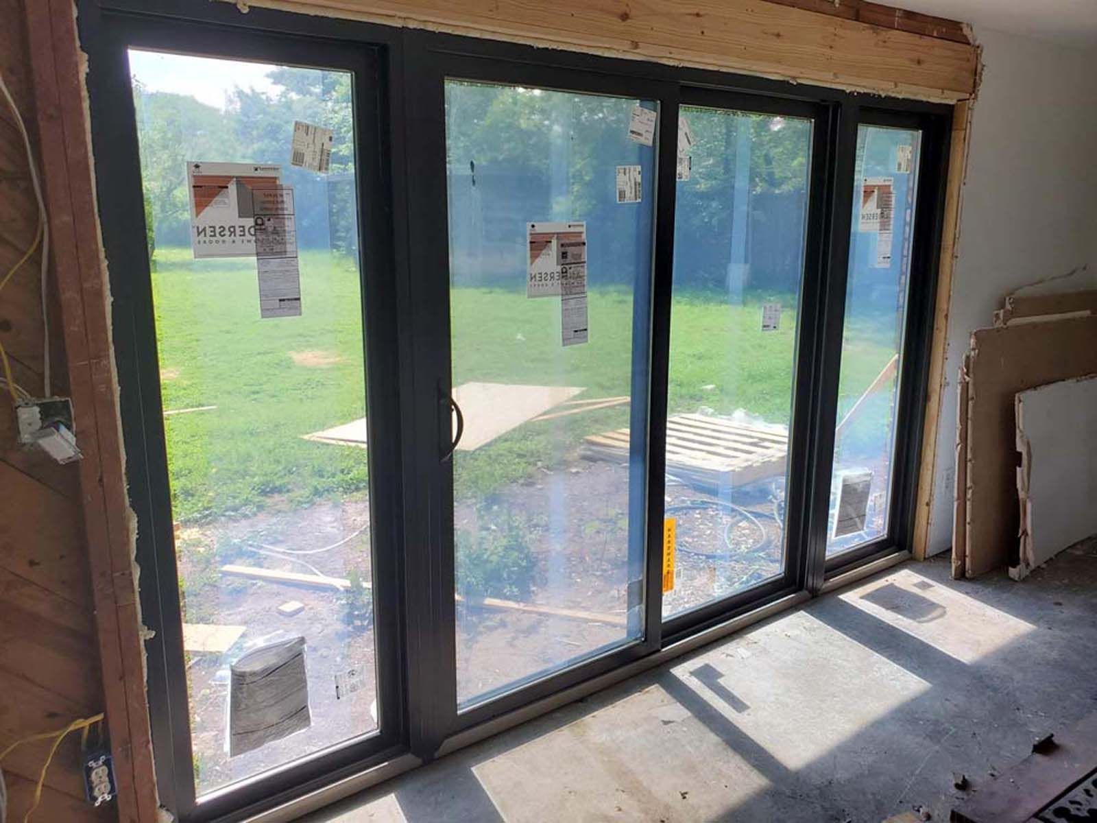 Large sliding glass doors installed in a home's frame, overlooking a green yard on a sunny day.