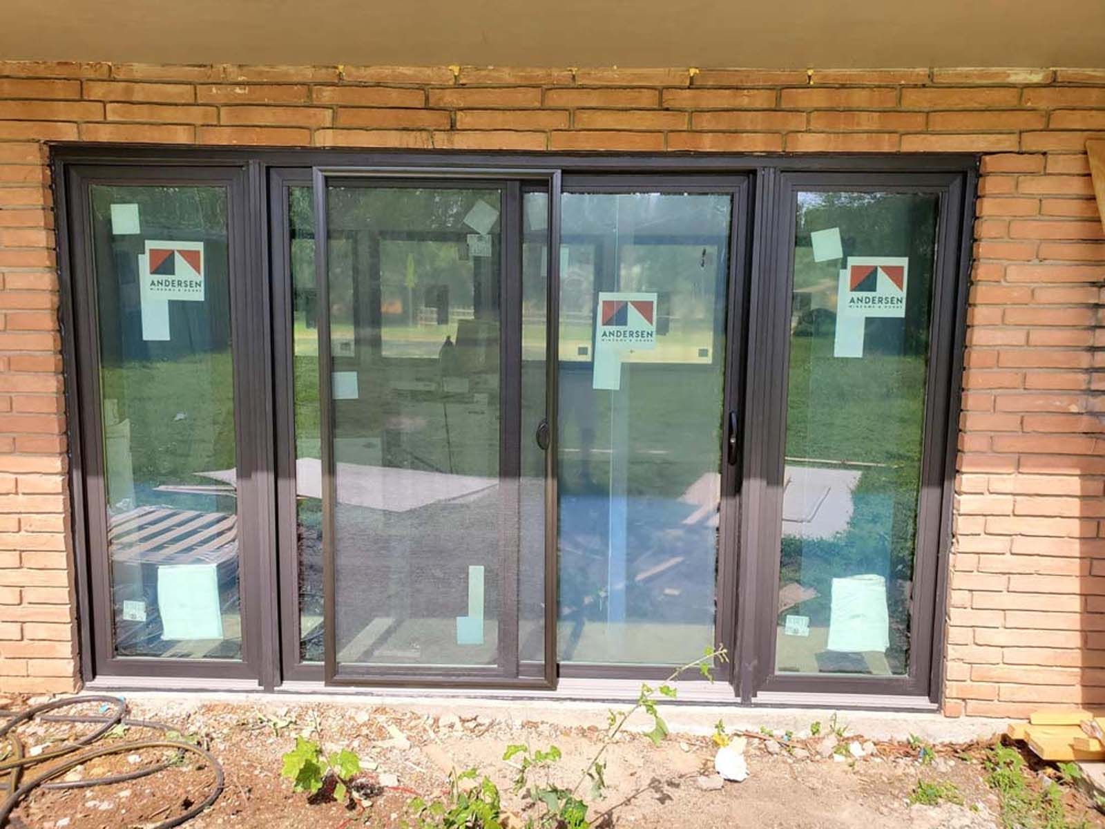 Dark-framed sliding glass doors installed in a brick wall, with protective paper still attached.
