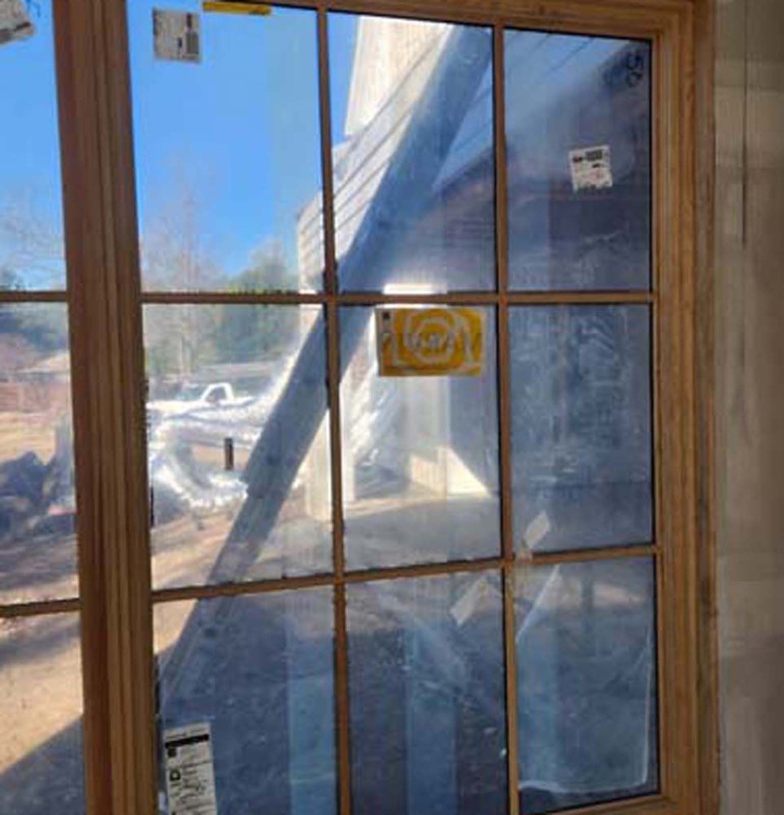 Window with multiple panes, view of a construction site with ladder and plastic sheeting.