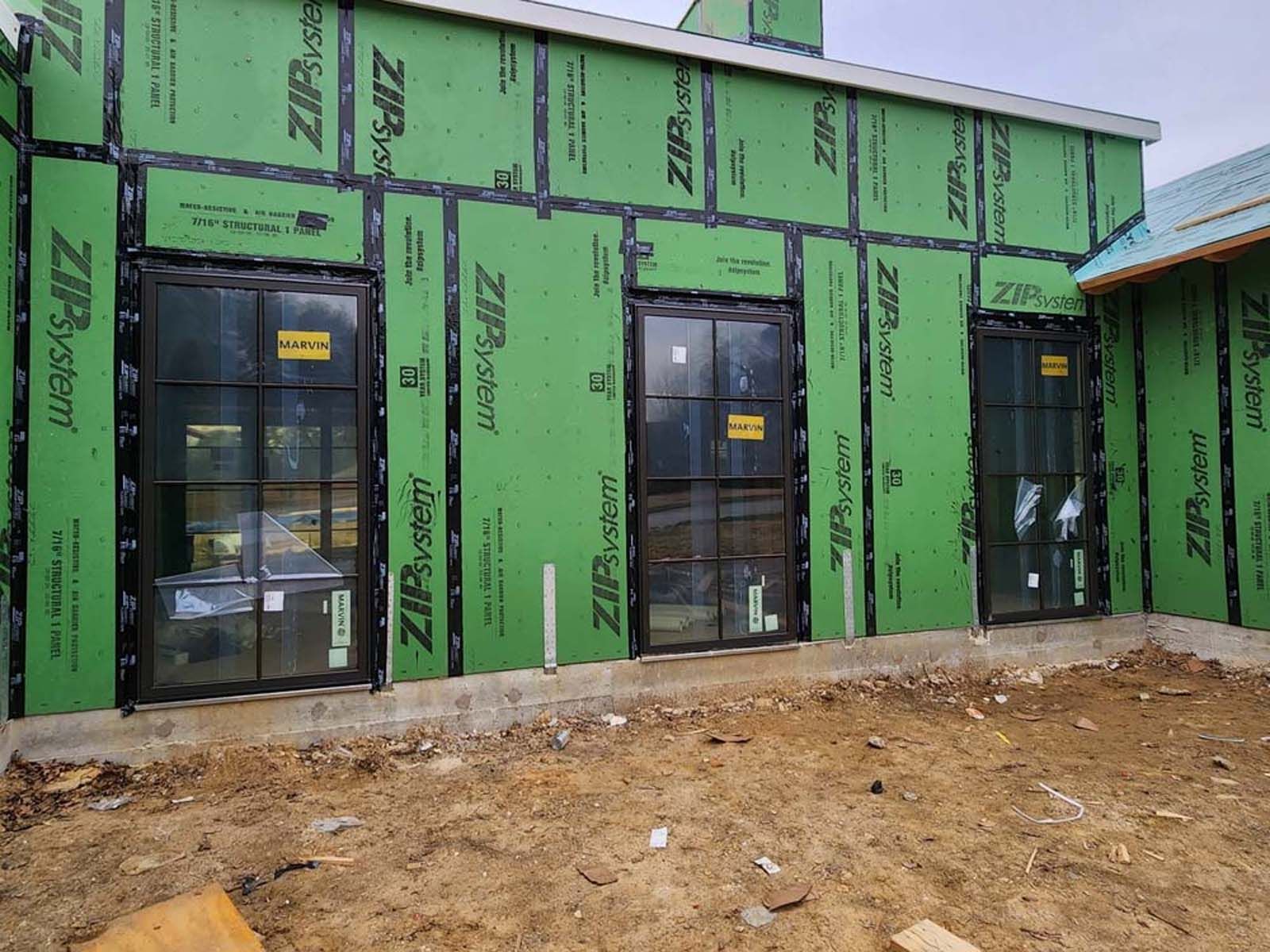 Exterior wall under construction with black framed windows, covered in green sheathing.