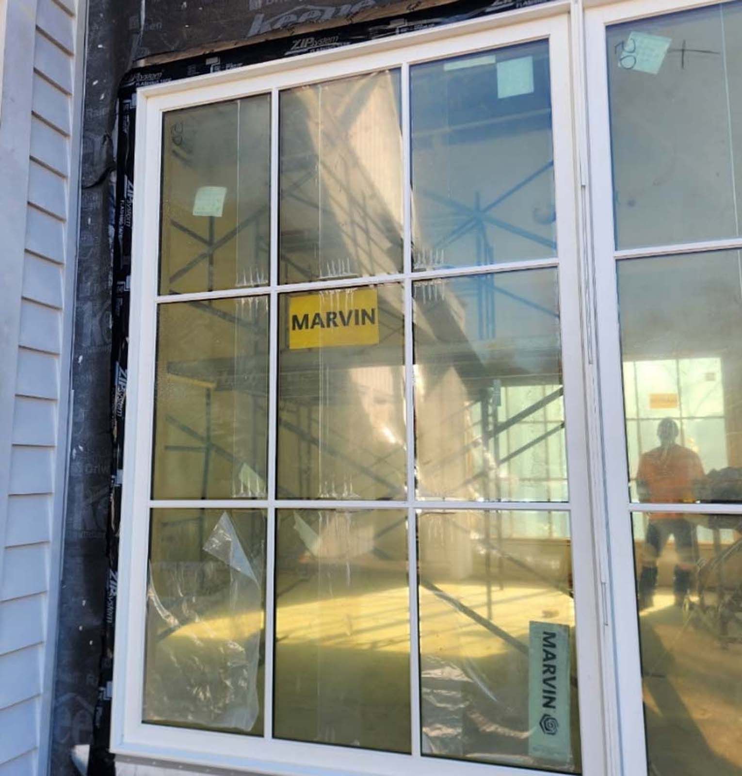 White-framed window with multiple panes under construction; a worker stands outside the window.