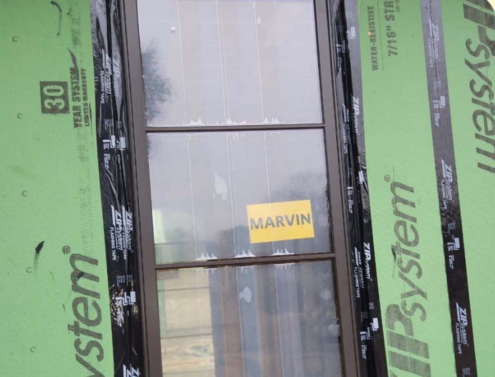 Brown window with Marvin sticker, installed between green sheathing and black sealant tape.