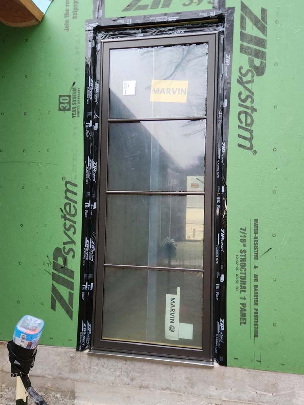 Brown window installed in a green Zip System wall. Black flashing tape is around the frame.