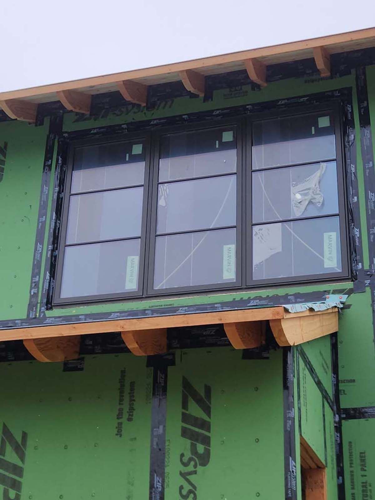 Black window in a house under construction; wood trim and green sheathing visible.