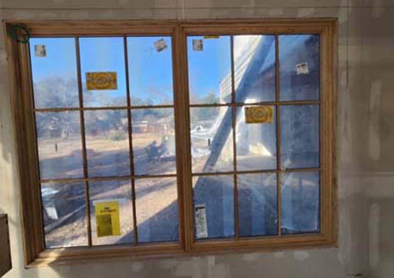 Double pane window with grid, reflecting blue sky and construction outside.