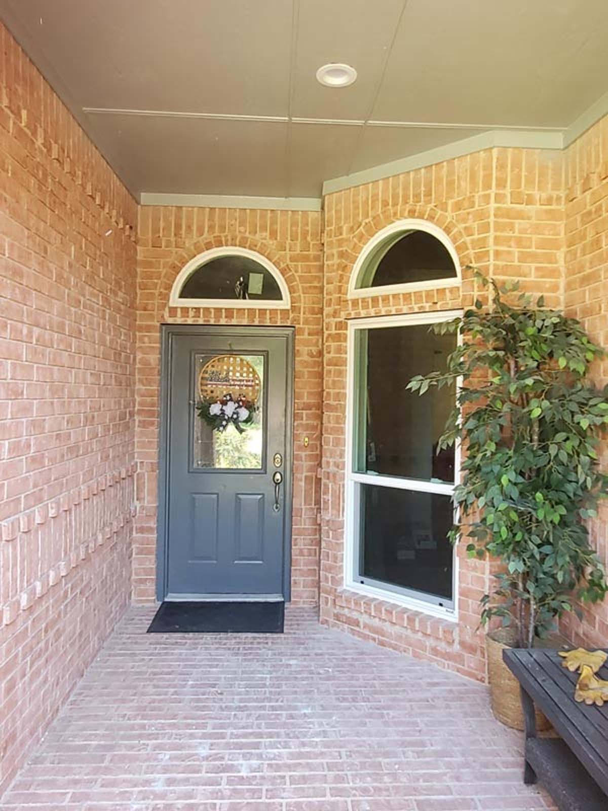 Brick front porch with gray door, arched window, and potted plant.