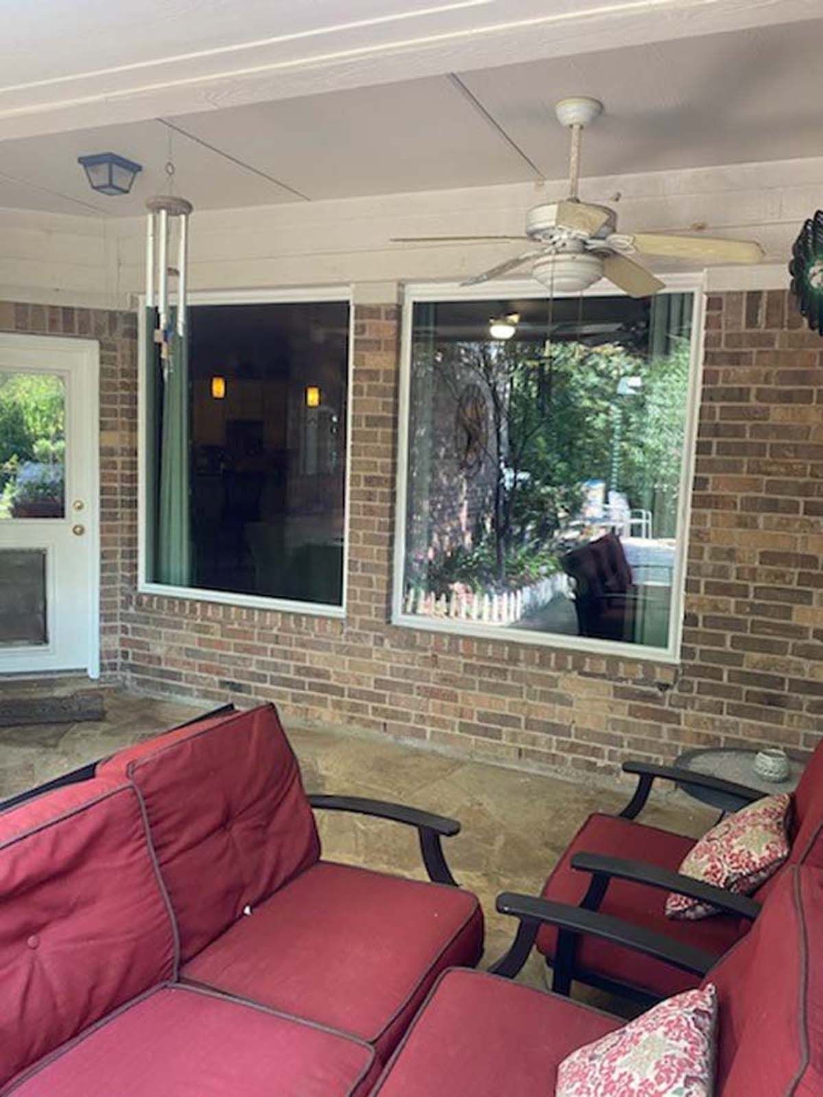 Covered patio with red sofas, brick wall, and large windows.  A ceiling fan and wind chimes are also visible.