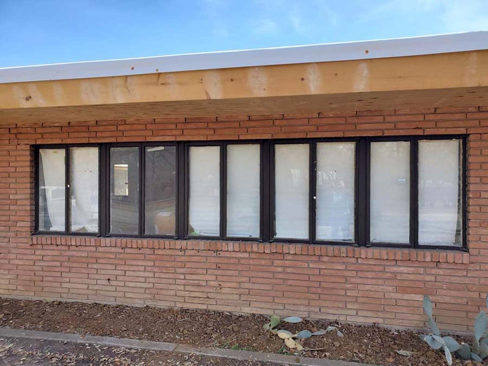 Brick building with a row of windows, white blinds, and dark frames, under a light-colored overhang.