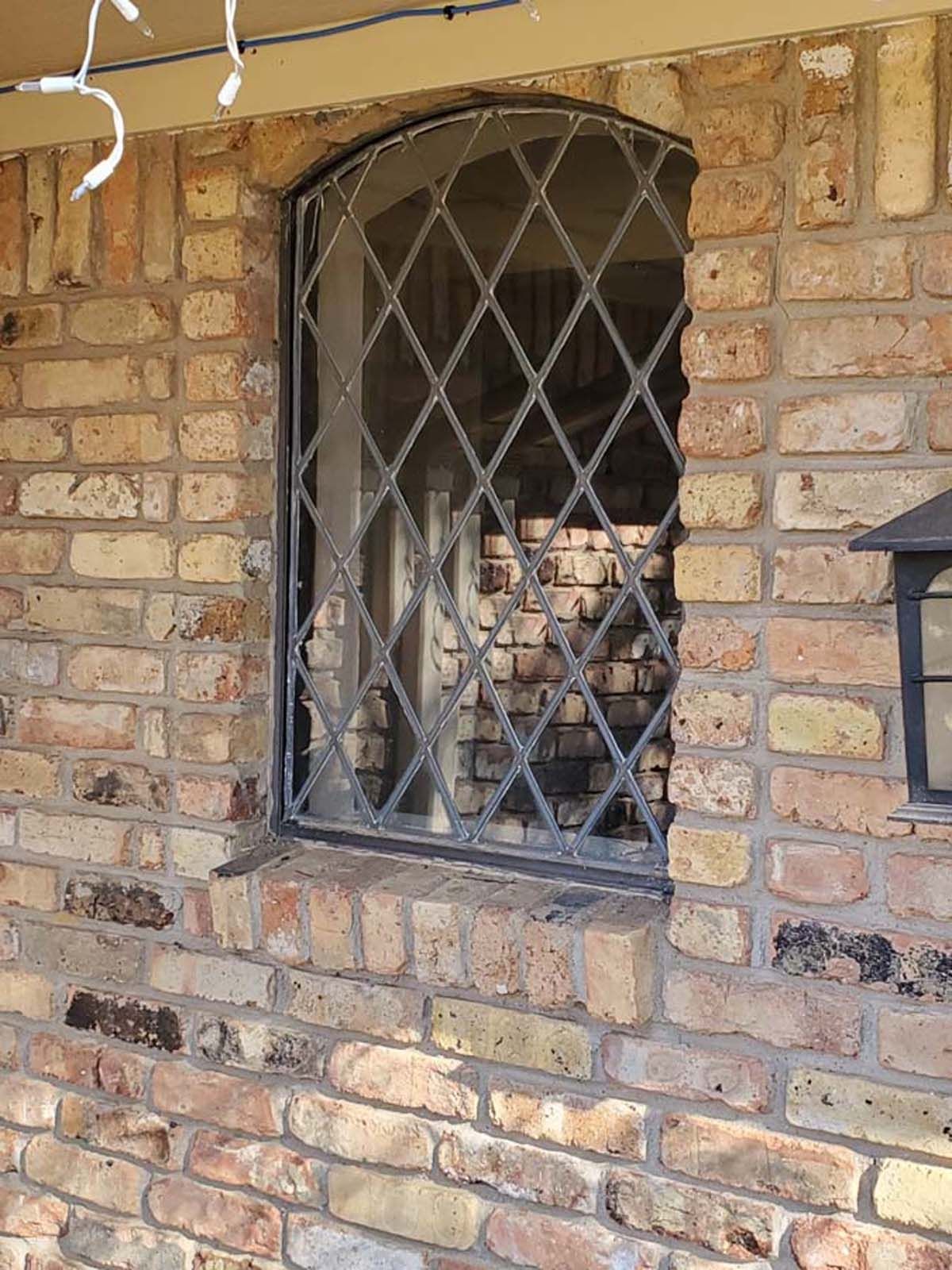 Brick building with arched window featuring diamond-patterned metal security bars.