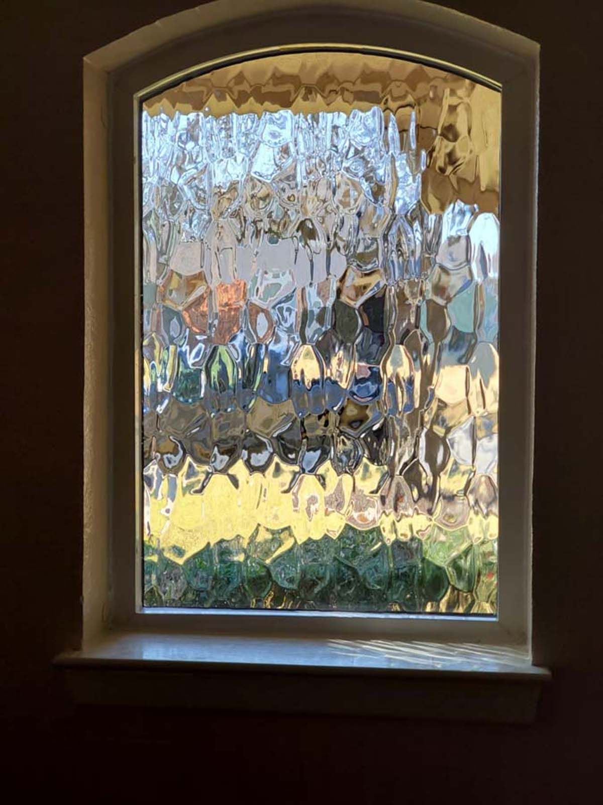 Window with textured glass, arch top, white frame. View outside obscured with colorful shapes.