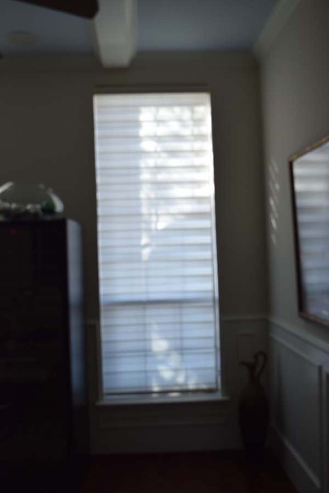 Window with horizontal blinds letting in light, beside a dark cabinet and a wall with a framed item.