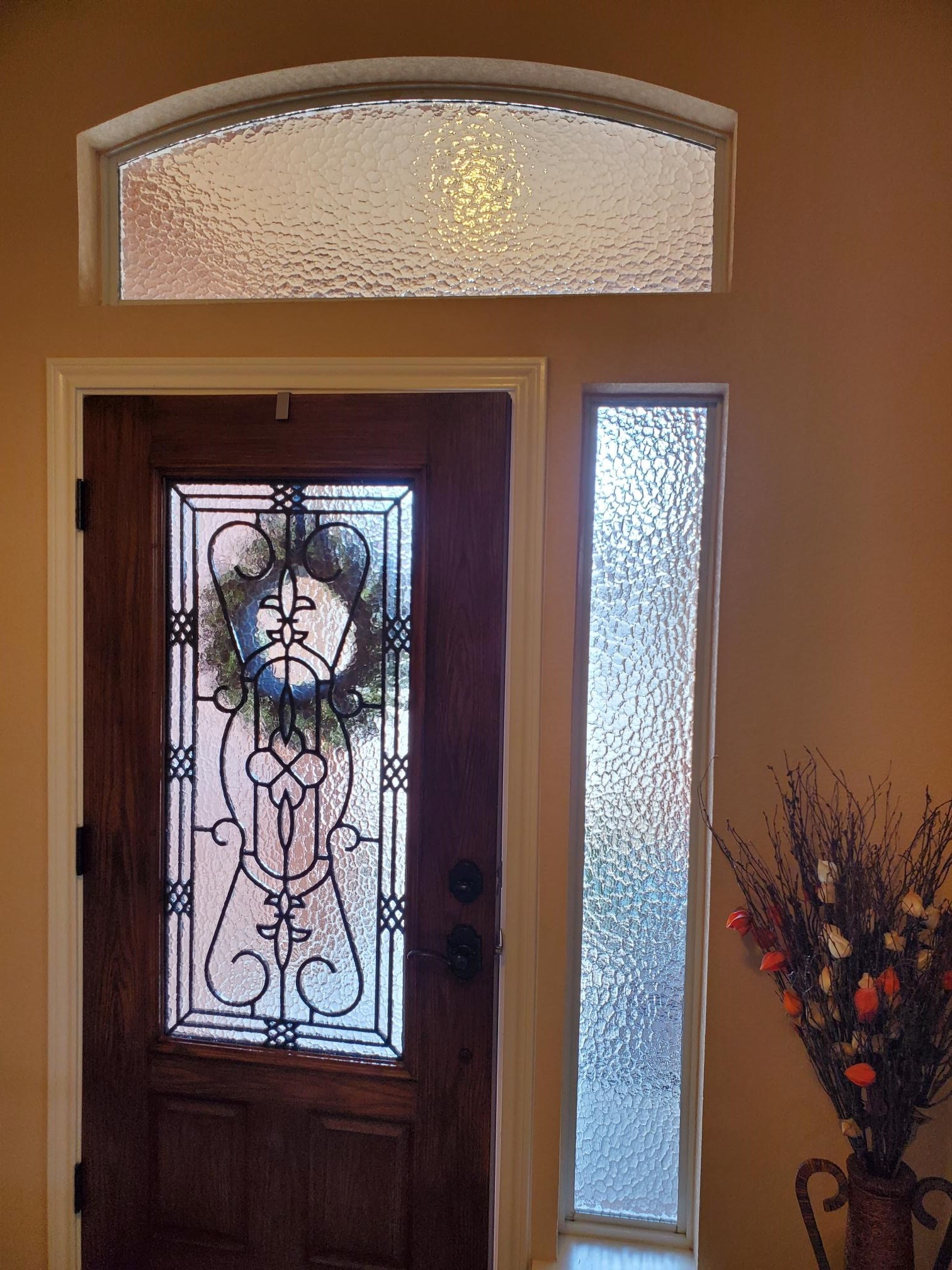 Wooden front door with decorative glass panels, sidelight, and arched transom, all with textured glass.