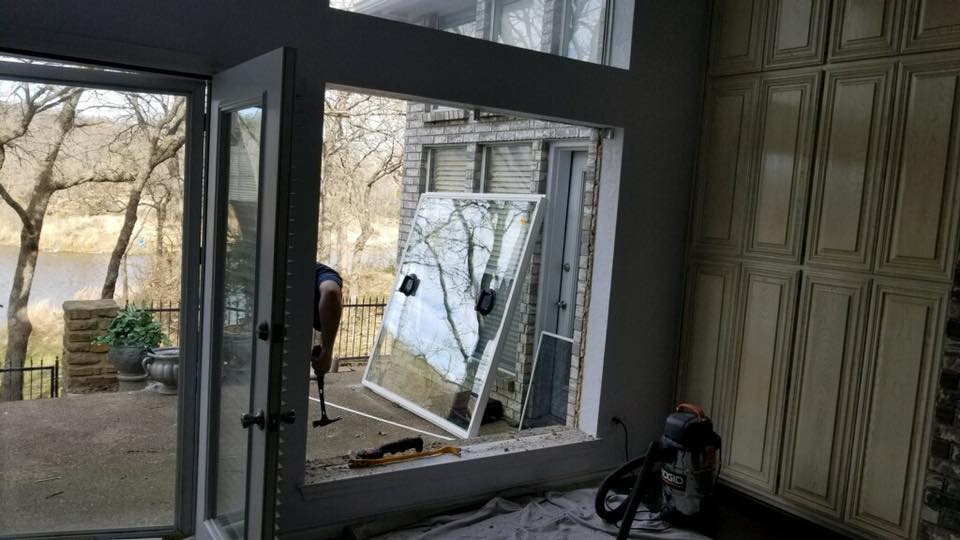 Interior view of a room with a large window being replaced, showing the outdoors and cabinets.