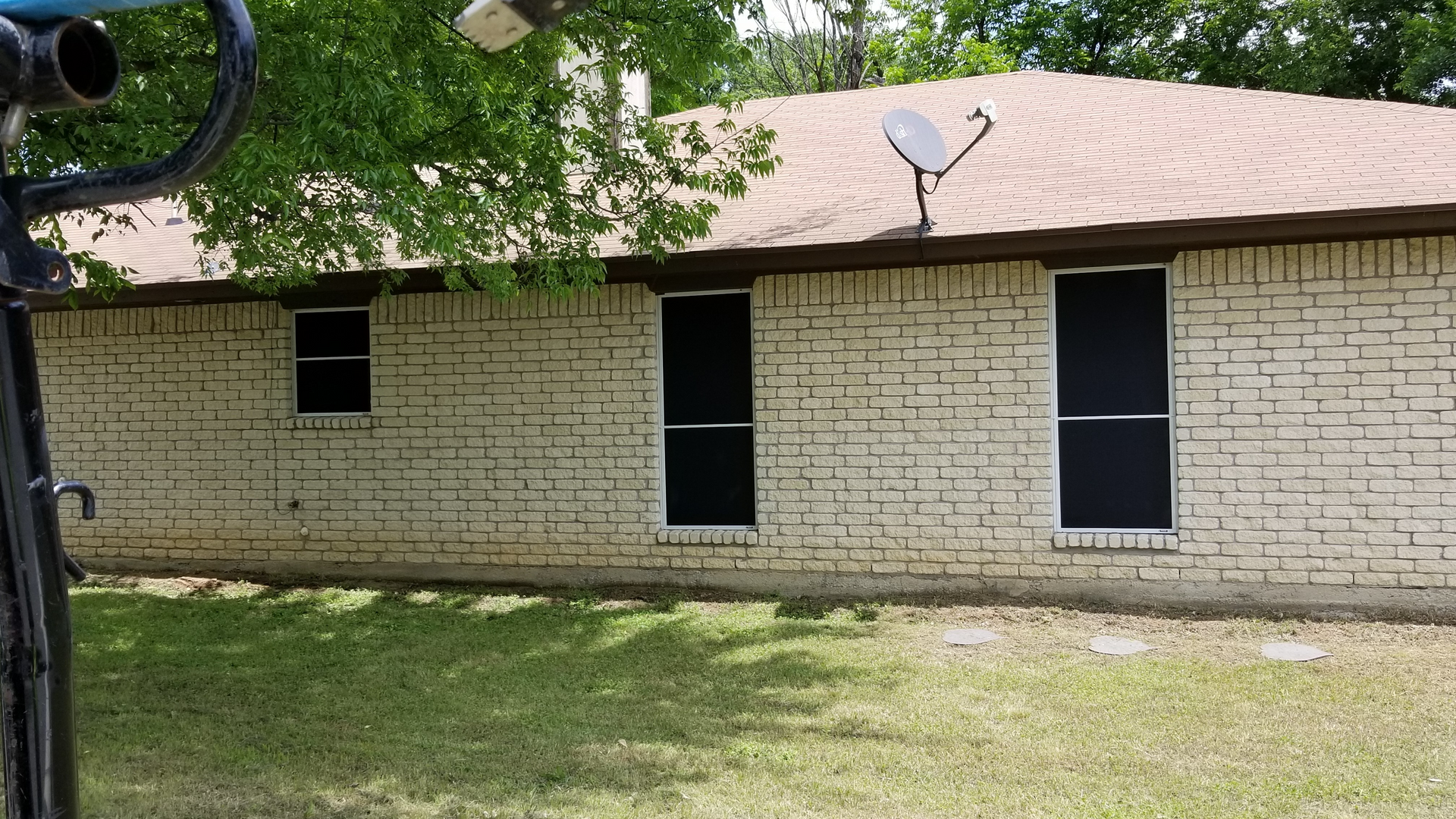 Tan brick house with three windows and a satellite dish on the roof.