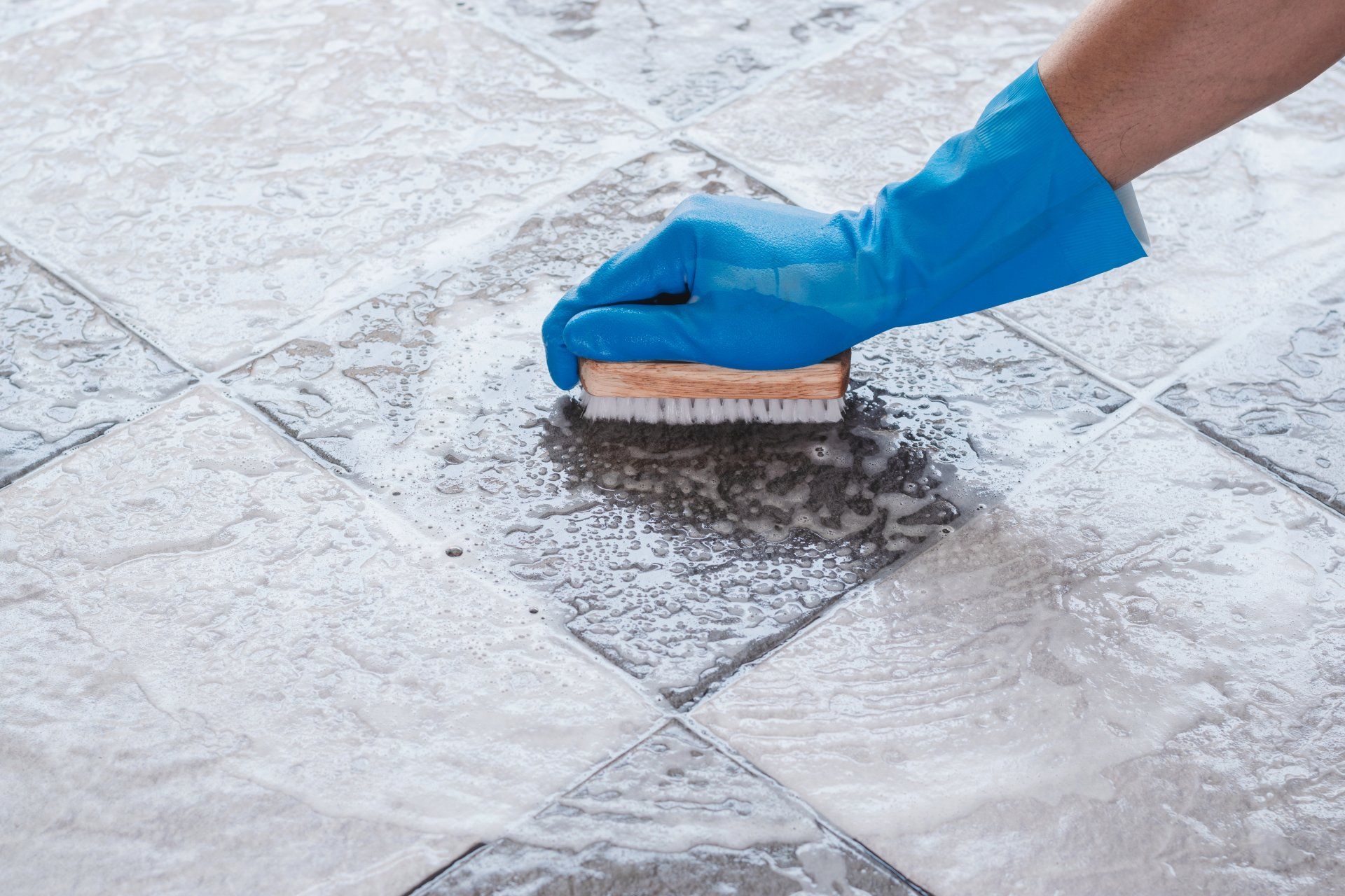 Hand of man wearing blue rubber gloves is used to convert scrub cleaning on the tile floor.