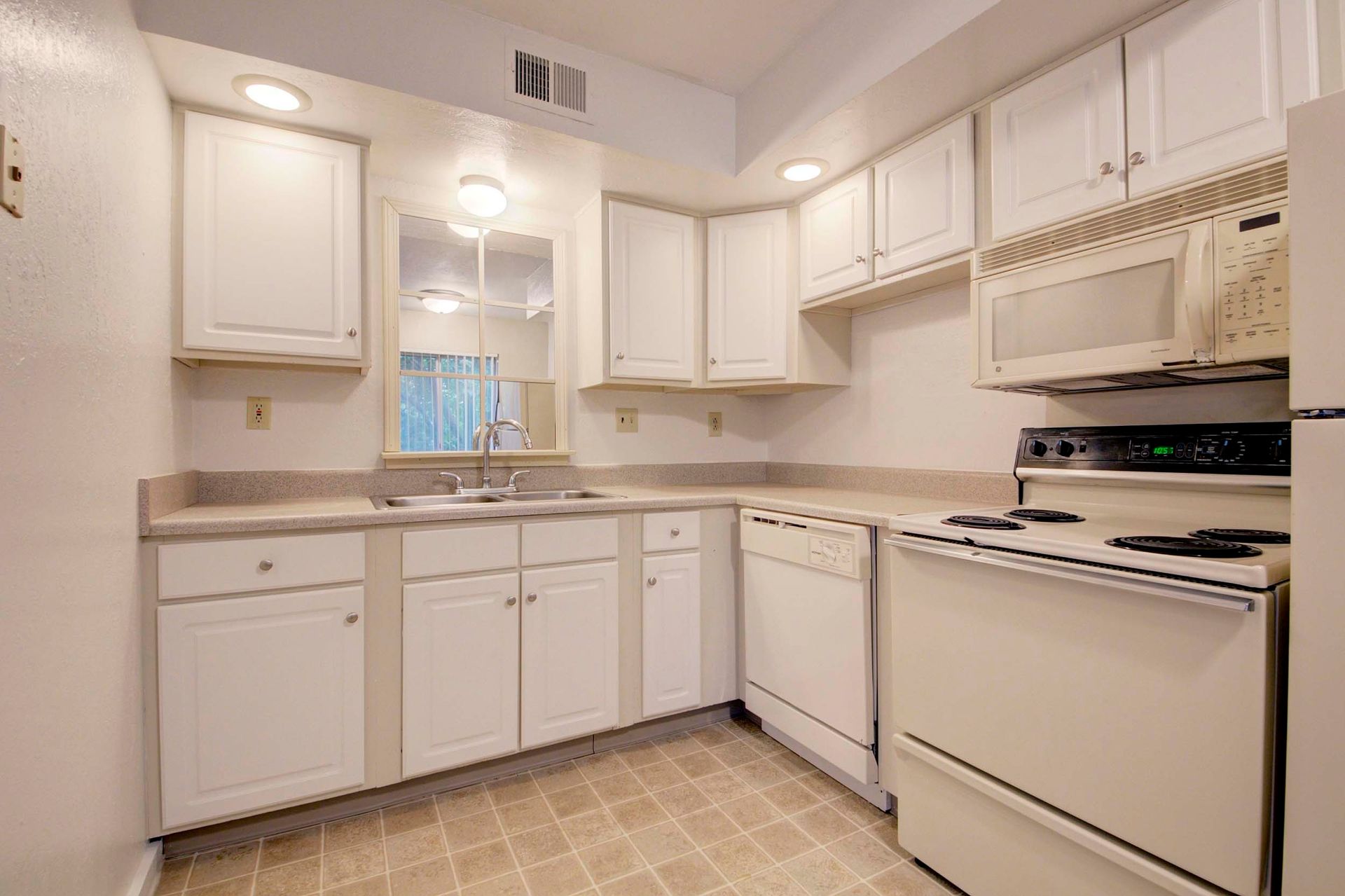 a kitchen with white cabinets , a stove , a refrigerator , and a microwave at Camelot Place.