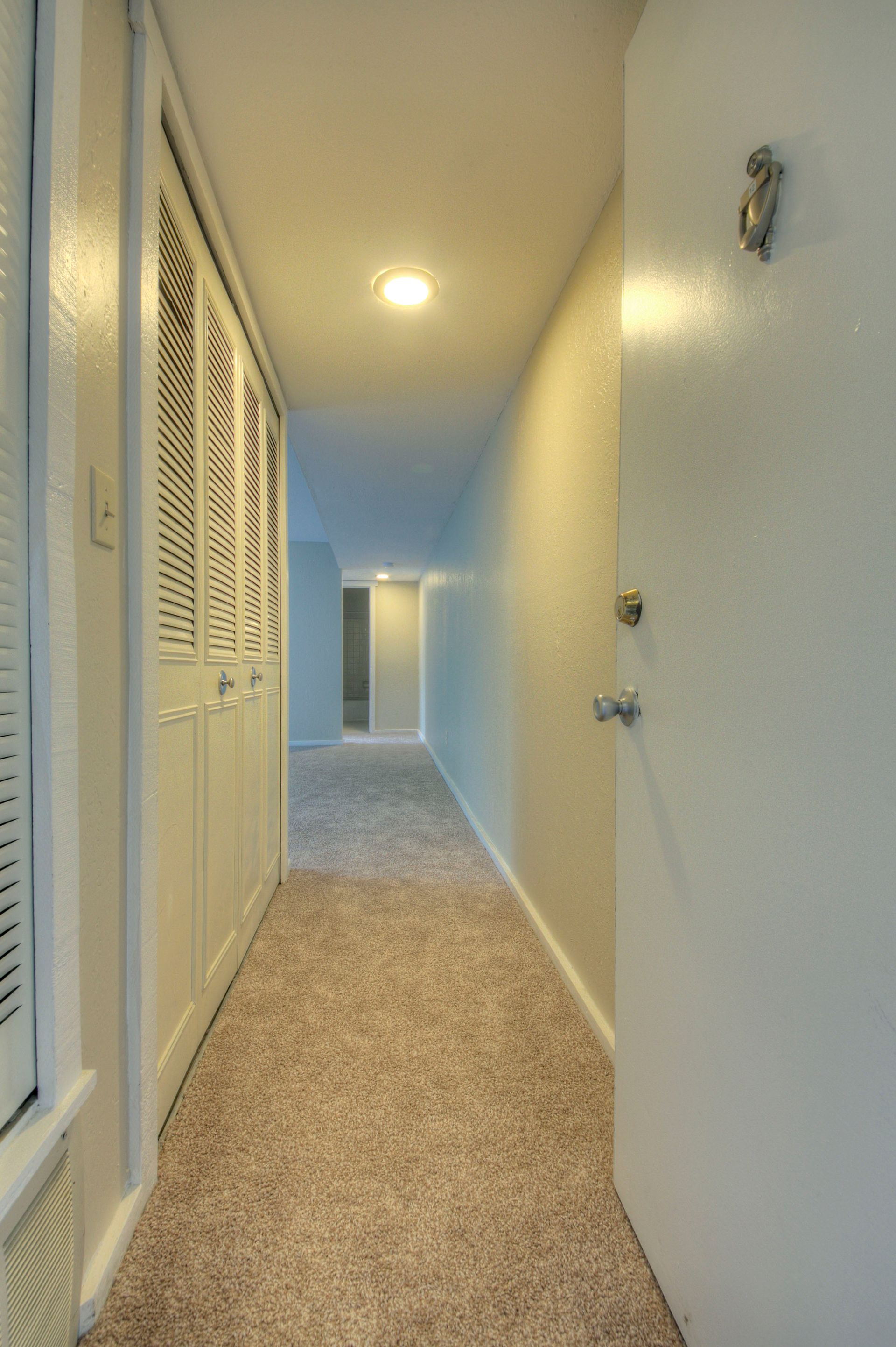 a hallway with a door that is open and a carpeted floor at Camelot Place.
