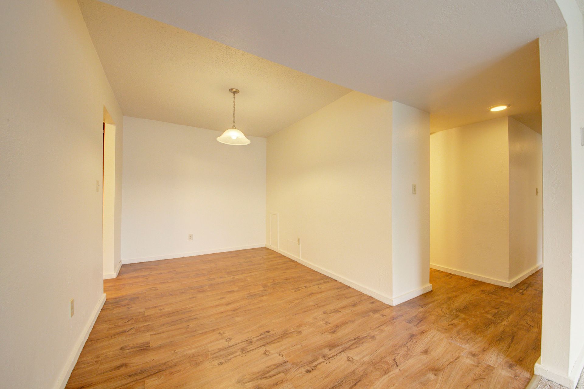 an empty living room with hardwood floors and white walls at Camelot Place.