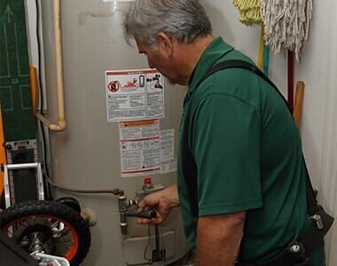 A man in a green shirt is working on a water heater.