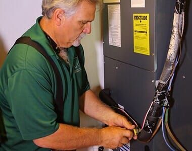 A man in a green shirt is working on an air conditioner.