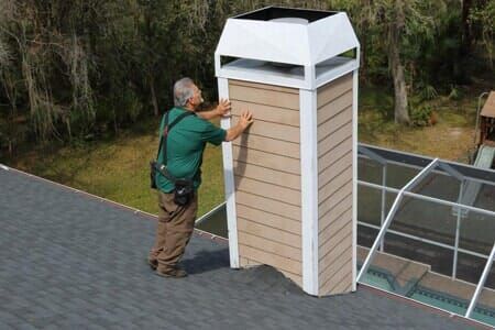 A man is standing on top of a roof fixing a chimney.