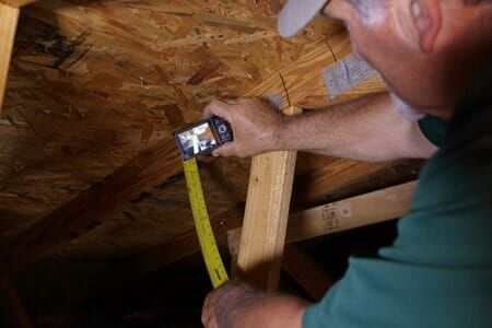 A man is measuring a piece of wood with a tape measure.