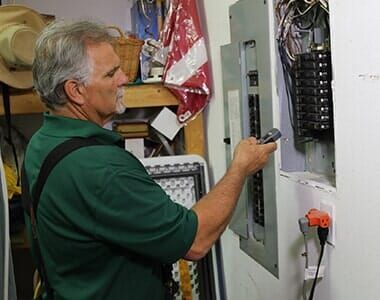 A man in a green shirt is working on an electrical box.