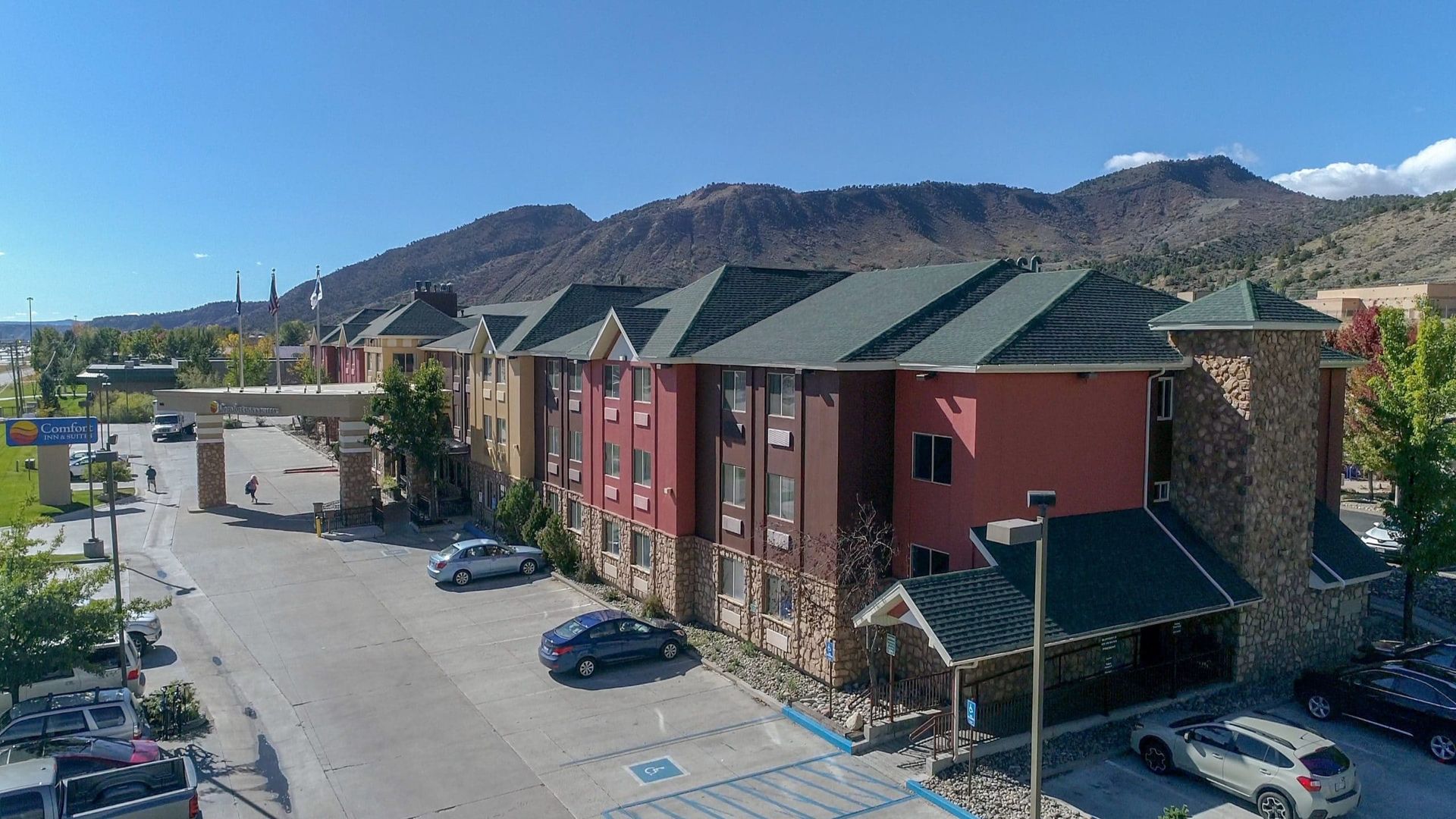An aerial view of a hotel with cars parked in front of it and mountains in the background.