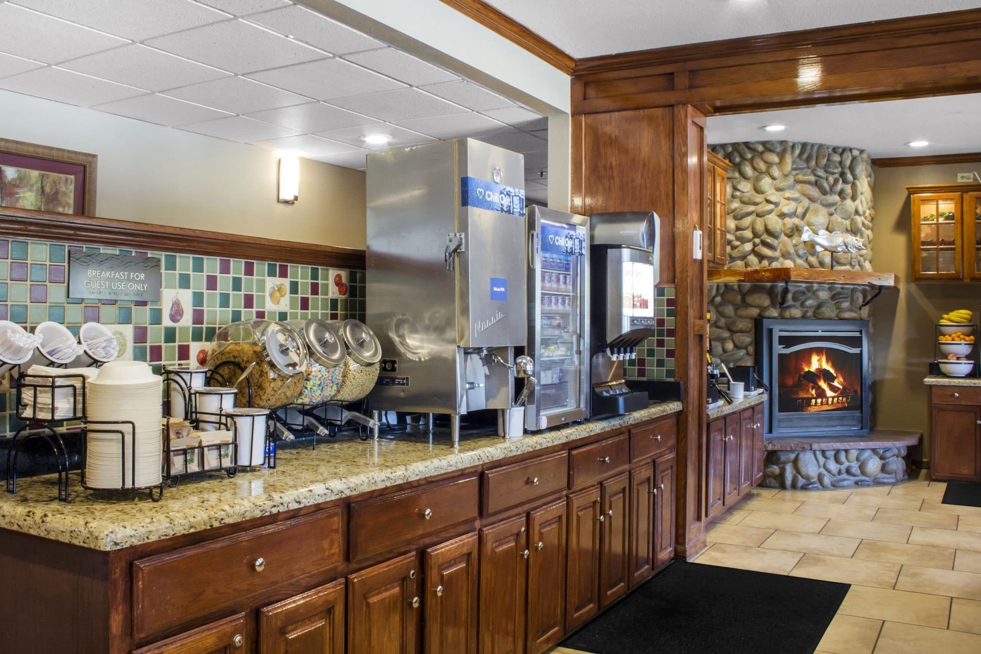 A kitchen with wooden cabinets , granite counter tops , a coffee maker and a fireplace.