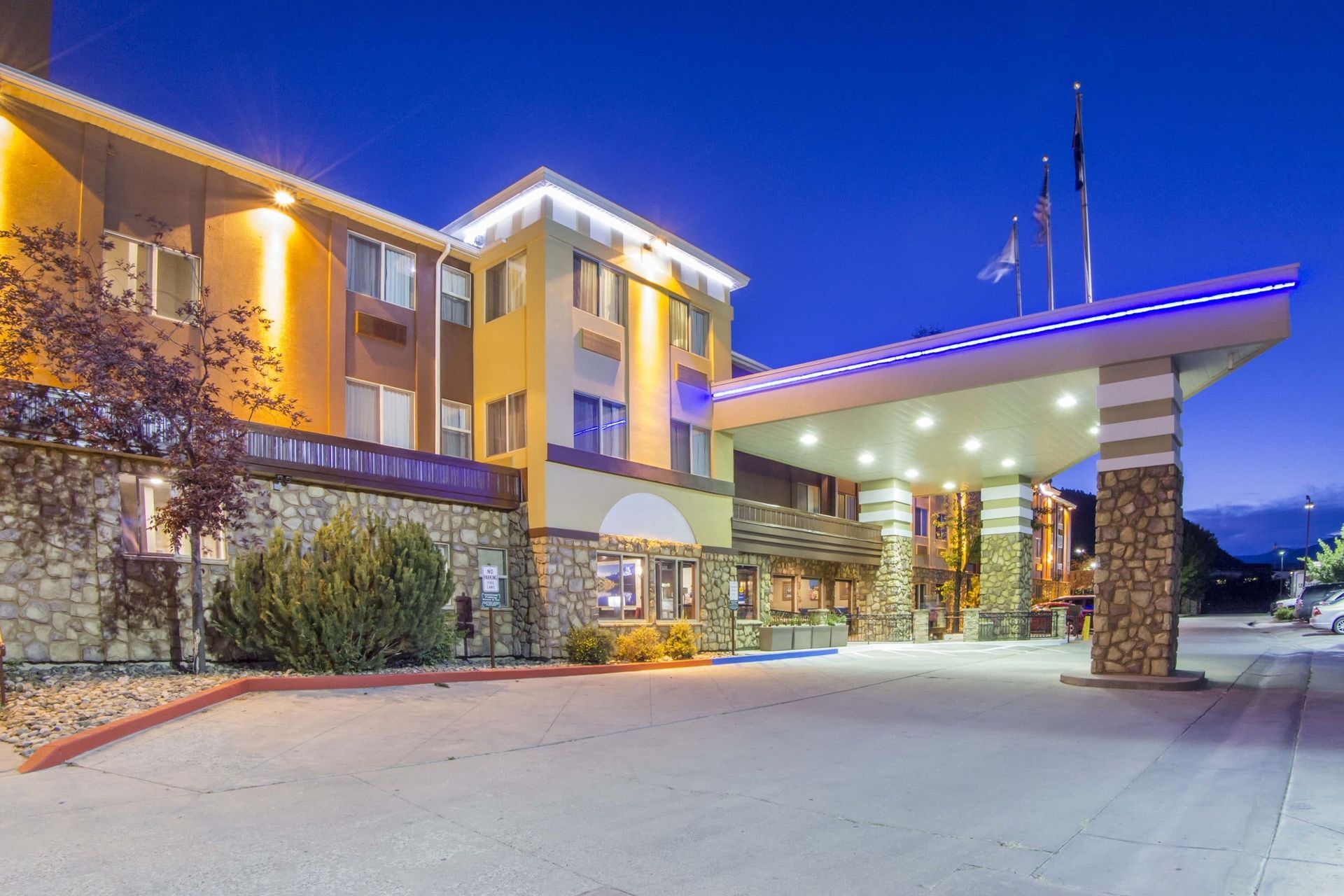 A large hotel building is lit up at night with a car parked in front of it.