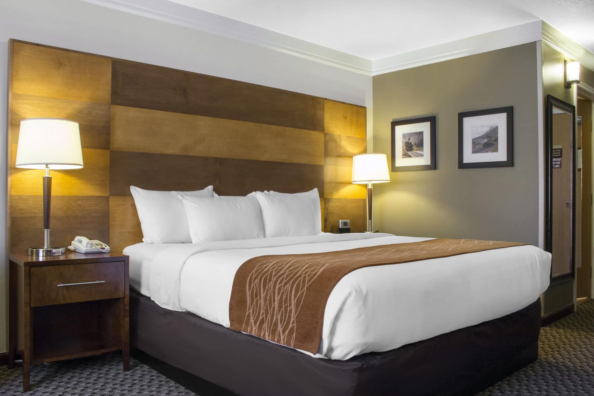 A hotel room with a king size bed , nightstand , lamps and pictures on the wall.
