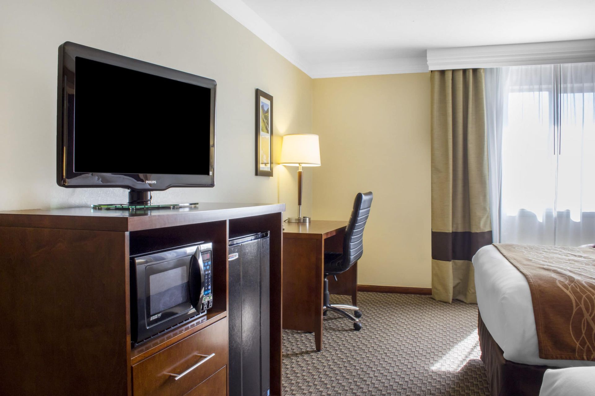 A hotel room with a bed , desk , television and microwave.