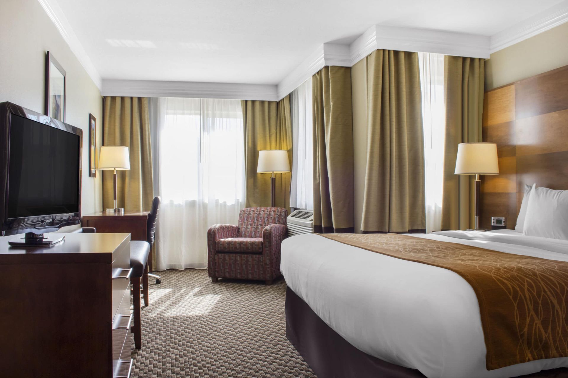 A hotel room with a king size bed , chair , desk and television.