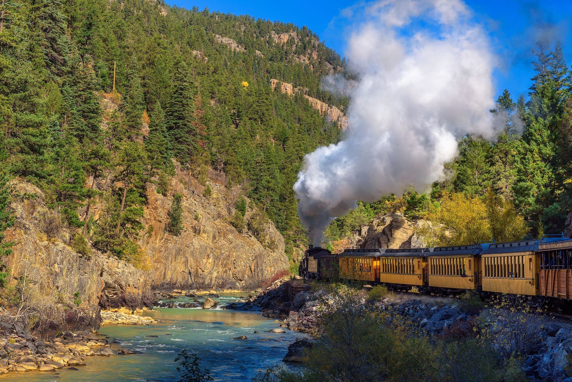 A train is going down a mountain next to a river.