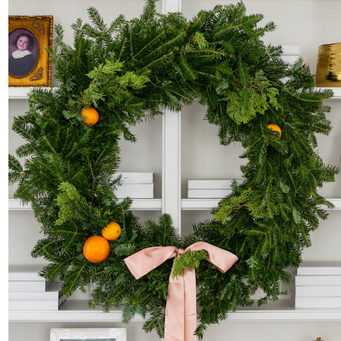 A christmas wreath with oranges and a pink bow