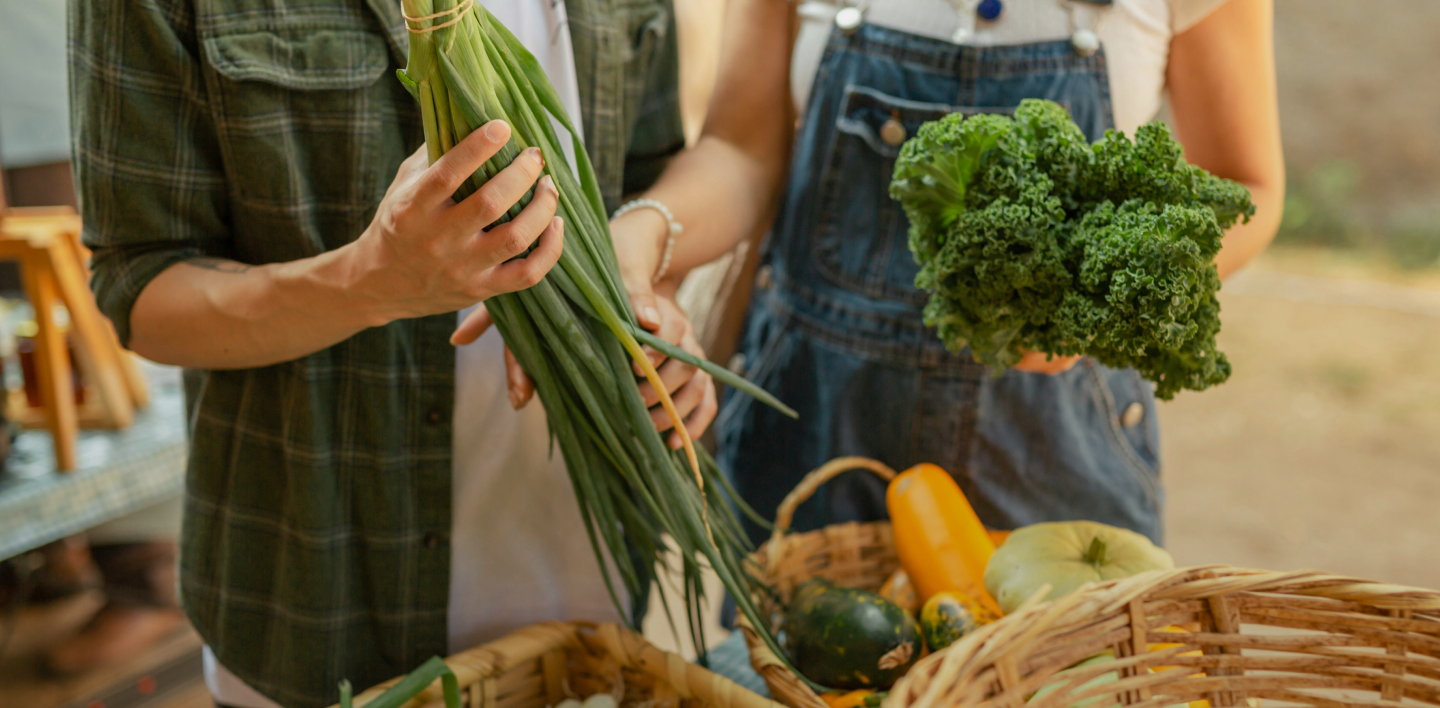 A man and a woman are standing next to each other holding vegetables.