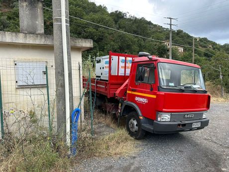 Un camioncino rosso con pianale ribassato è parcheggiato su una strada sterrata, accanto a un muro di cemento e a un pendio.