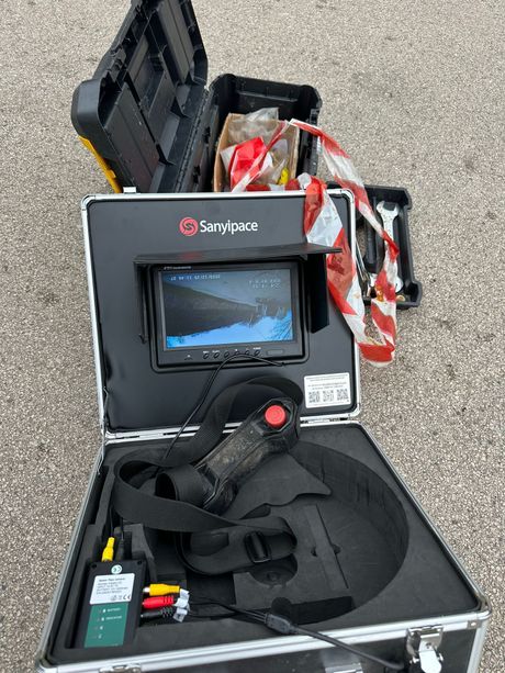 Valigetta nera aperta con monitor, cavi e accessori sul marciapiede.