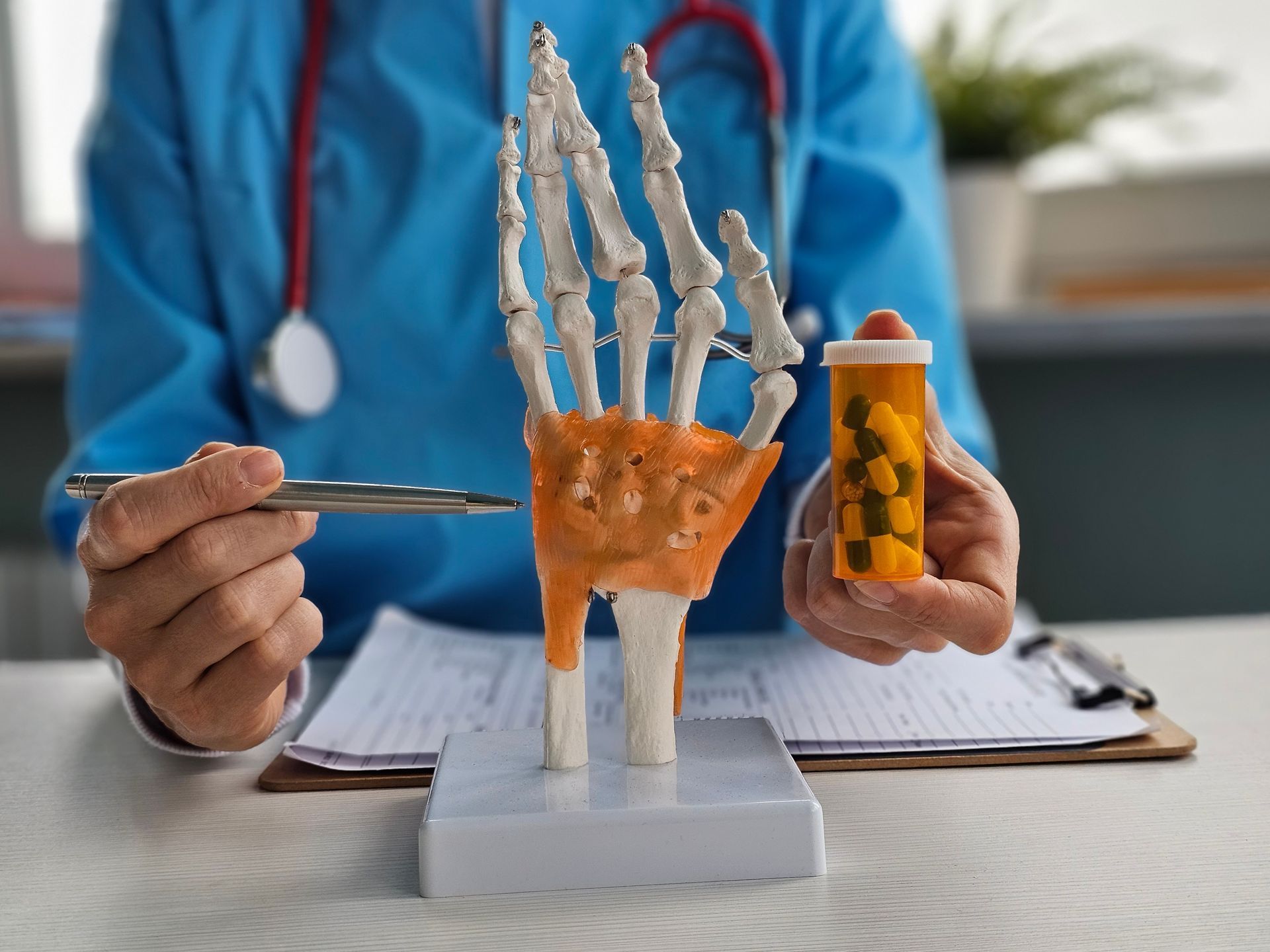 A doctor is holding a bottle of pills and a model of a hand.