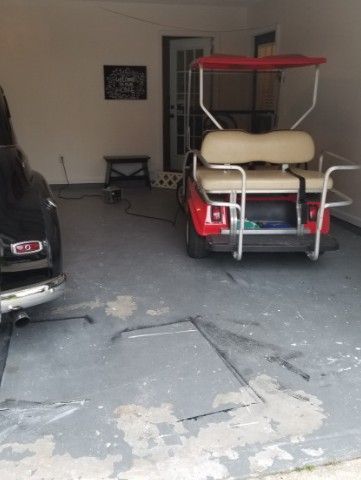 Covered golf cart parked in a garage beside a black car on a concrete floor